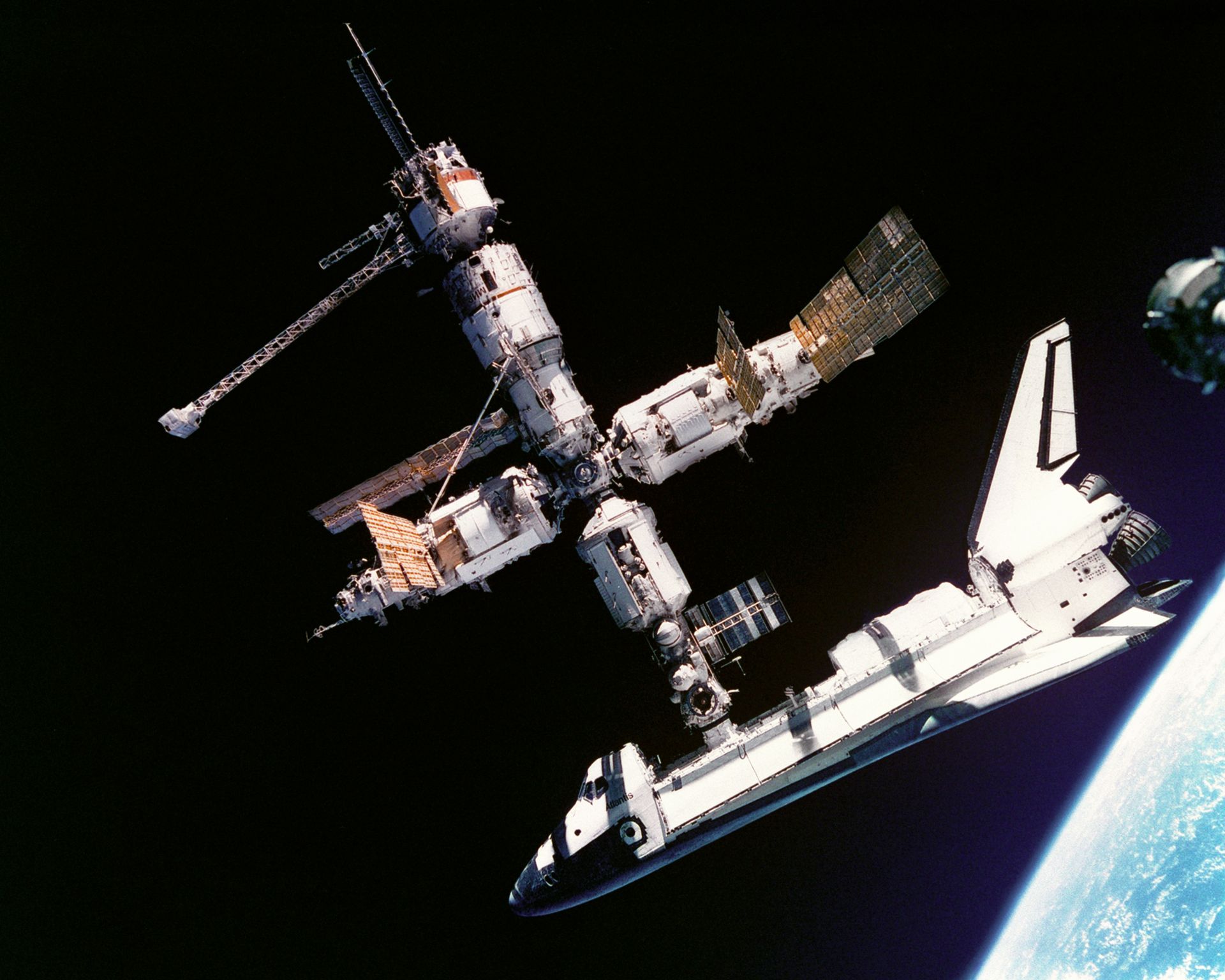 El Atlantis atracado en la Mir en julio de 1995, y abajo a la derecha asoma la Tierra